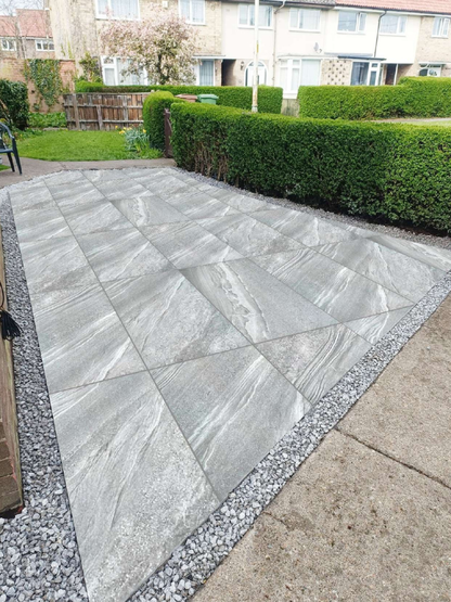 Gray stone patio in a residential garden with greenery and houses in the background