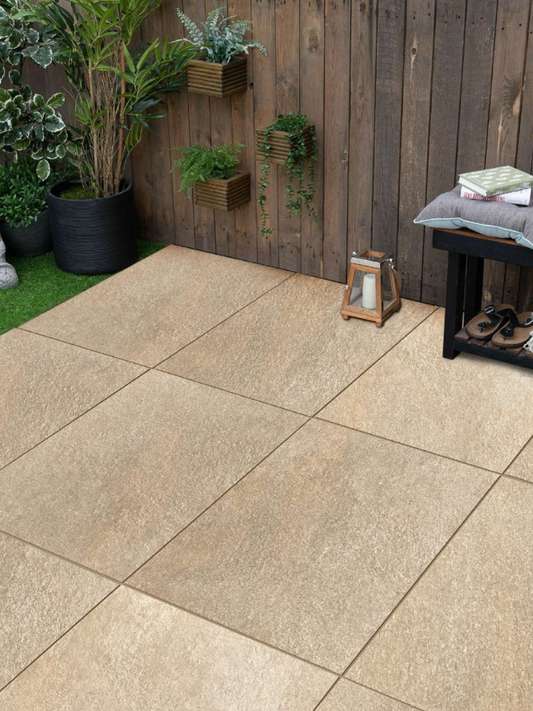 Beige patio tiles in a garden setting with plants and a wooden wall.