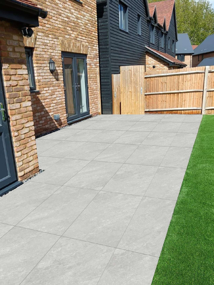 Paved patio area in front of a house with a wooden fence and grass